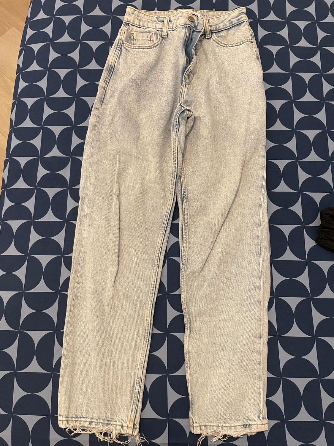 Light wash denim jeans with a frayed hem, placed on top of a blue and grey geometric patterned fabric.