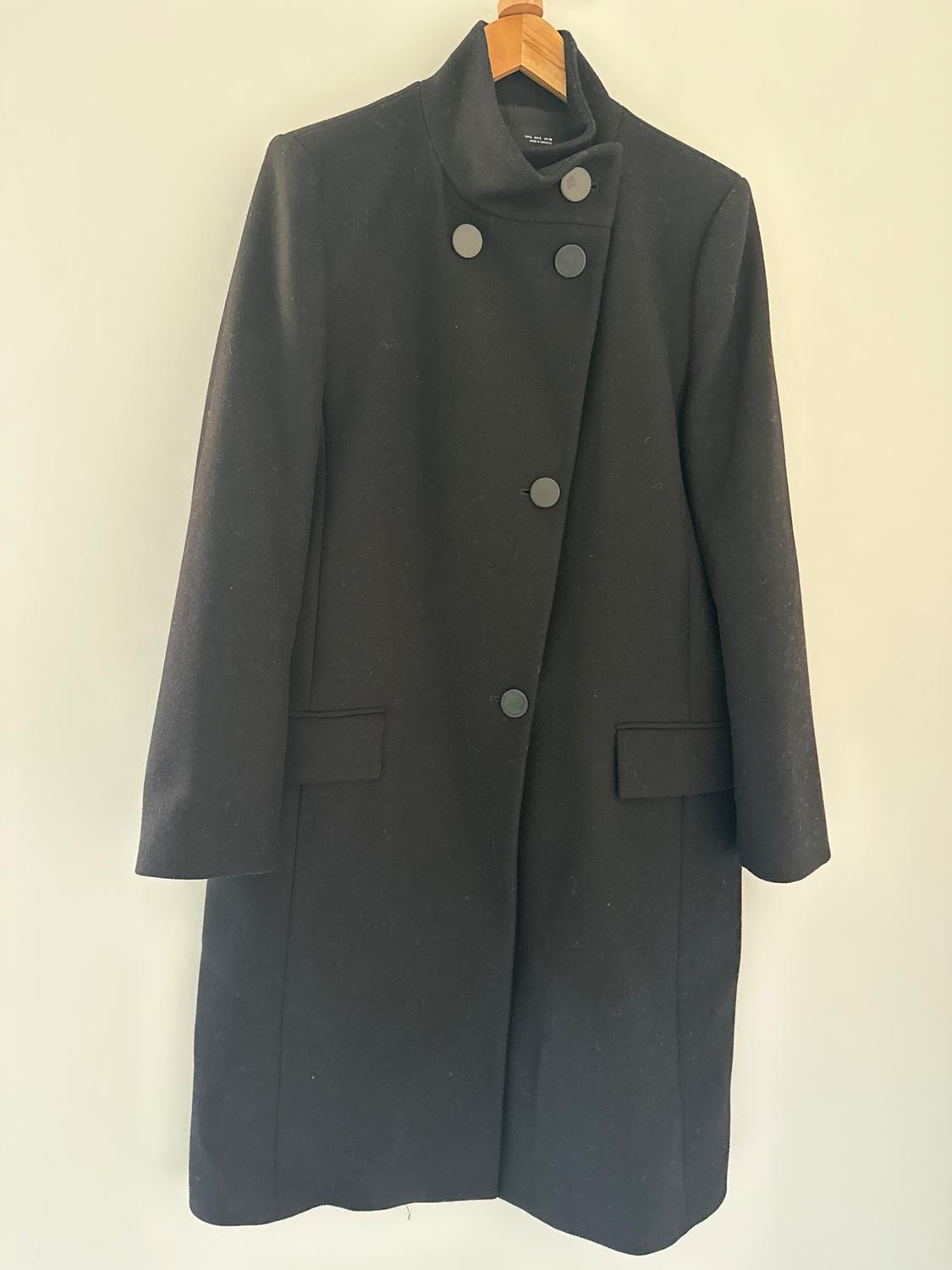 Black wool coat with a high collar and double-breasted closure, hanging on a wooden hanger against a white background.