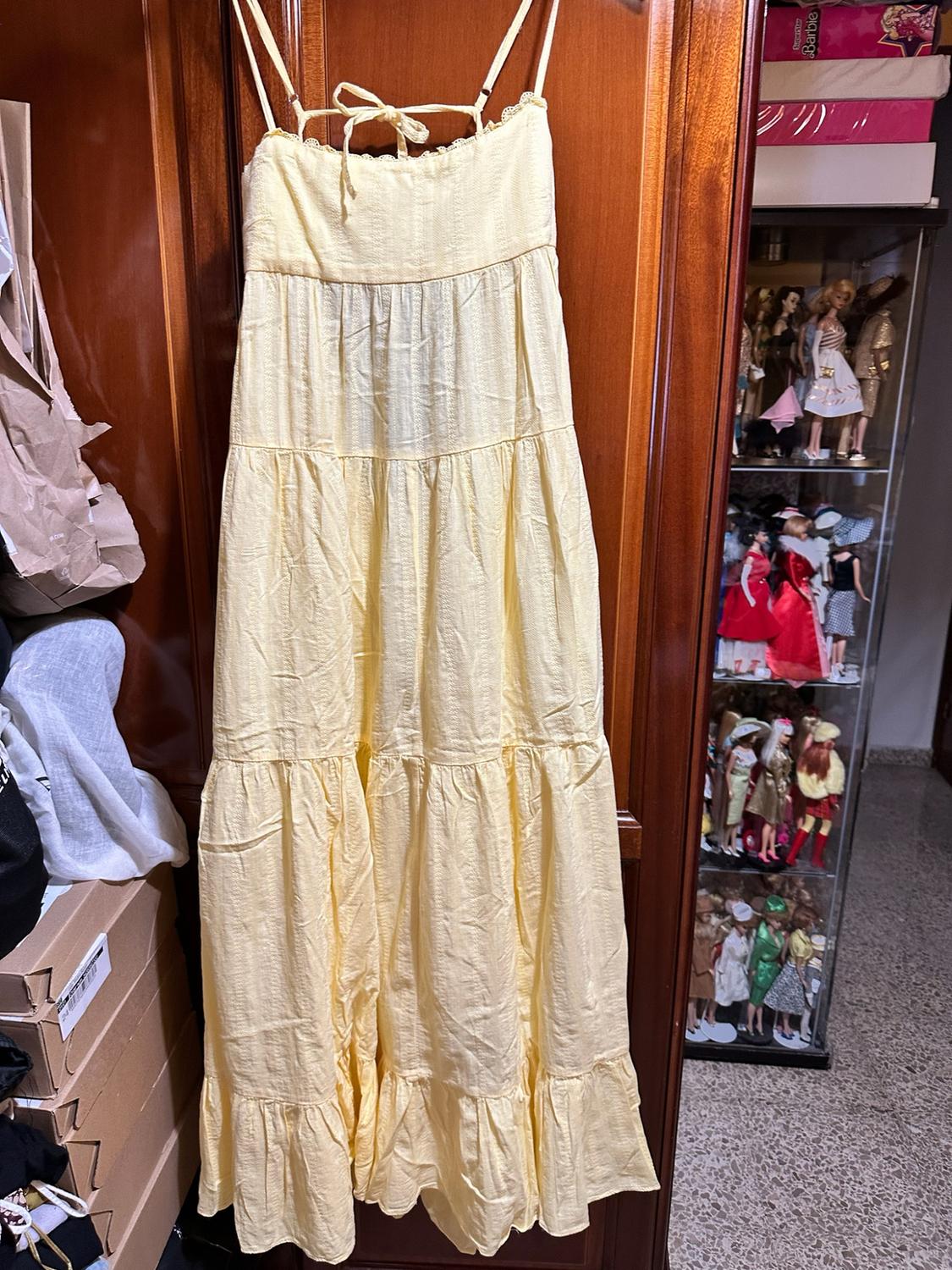 Long yellow ruffled dress hanging in a wardrobe. Next to it, a display cabinet with dolls and a box with the text Superstar Barbie.