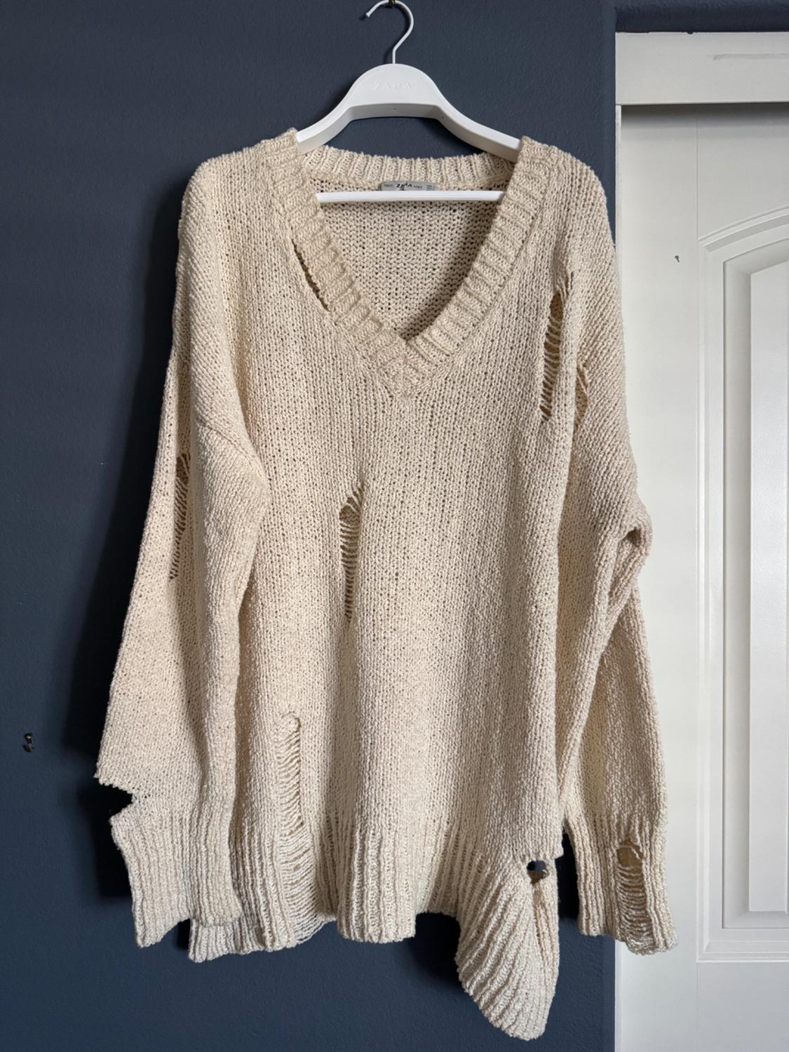 Front view of a beige V-neck sweater with distressed details.