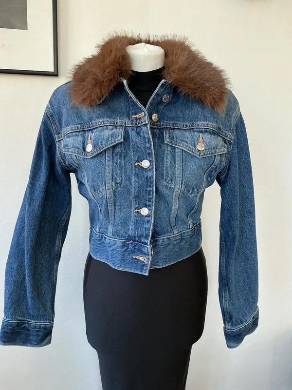 Blue denim jacket with a brown faux fur collar on a black mannequin
in front of a white wall.