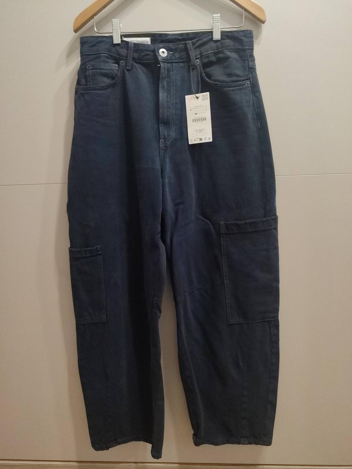 Dark blue cargo-style jeans with side pockets, hanging on a wooden hanger against a light background.