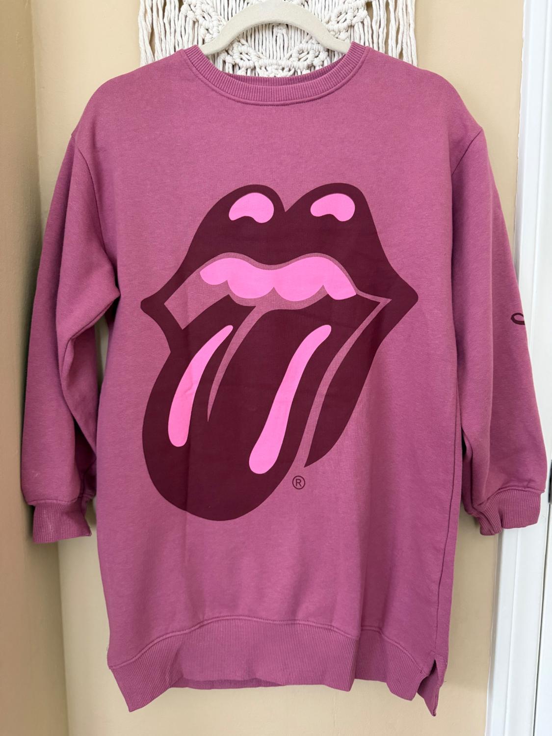 Pink sweatshirt with a mouth and tongue design in fuchsia and burgundy tones, hanging on a hanger against a beige background.