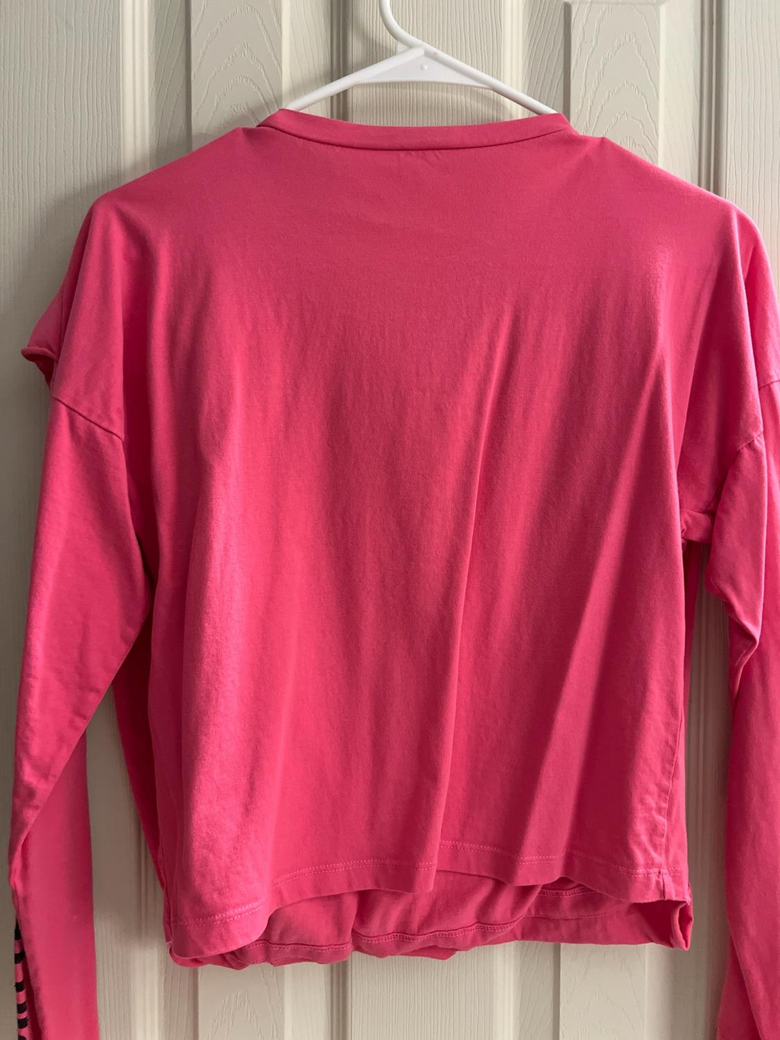 Pink long-sleeve shirt hanging on a hanger over a white door. Plain back view with a striped detail on the left cuff.