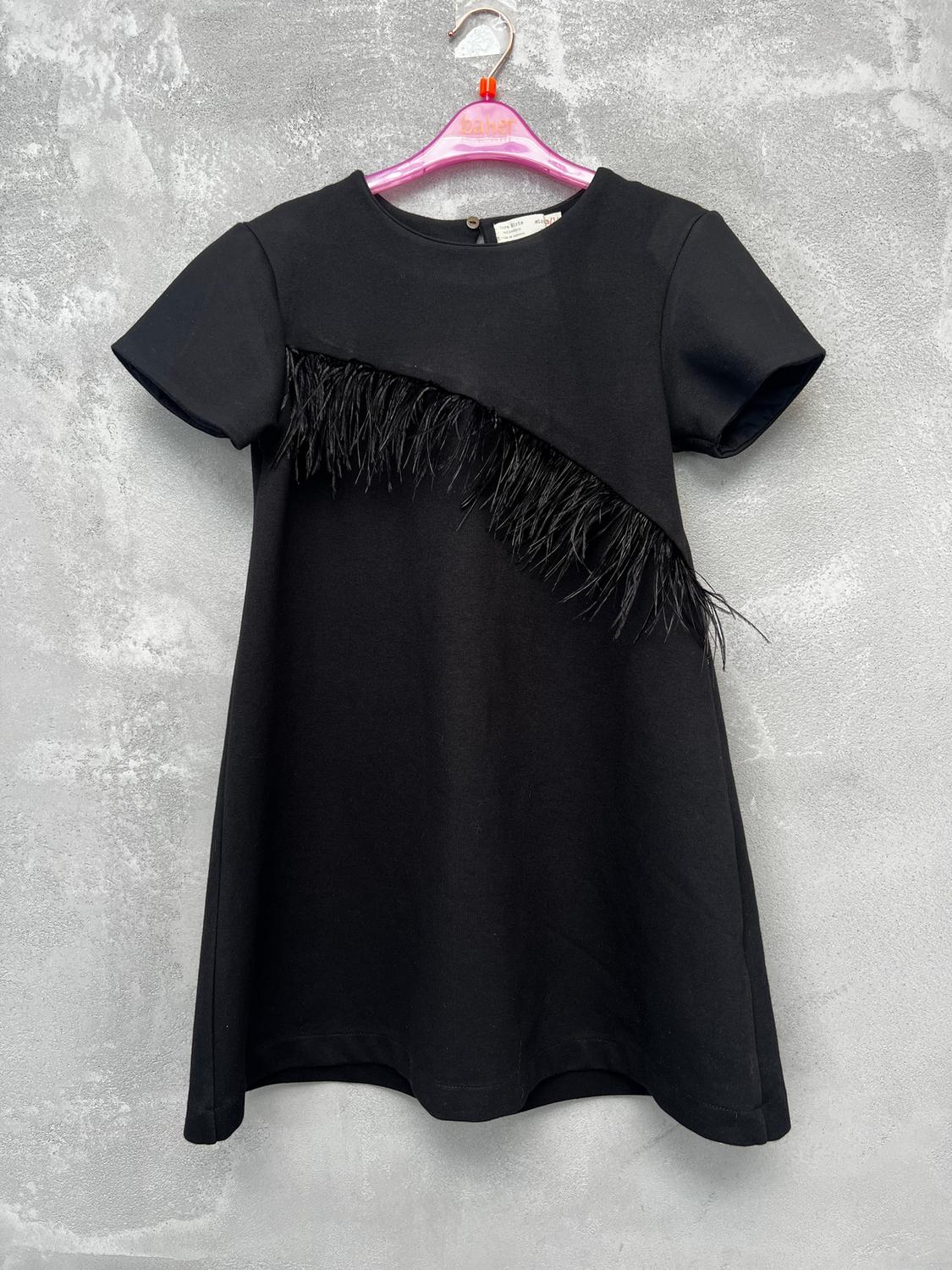 Black dress with diagonal fringe detail, hanging on a pink hanger against a textured grey wall background.