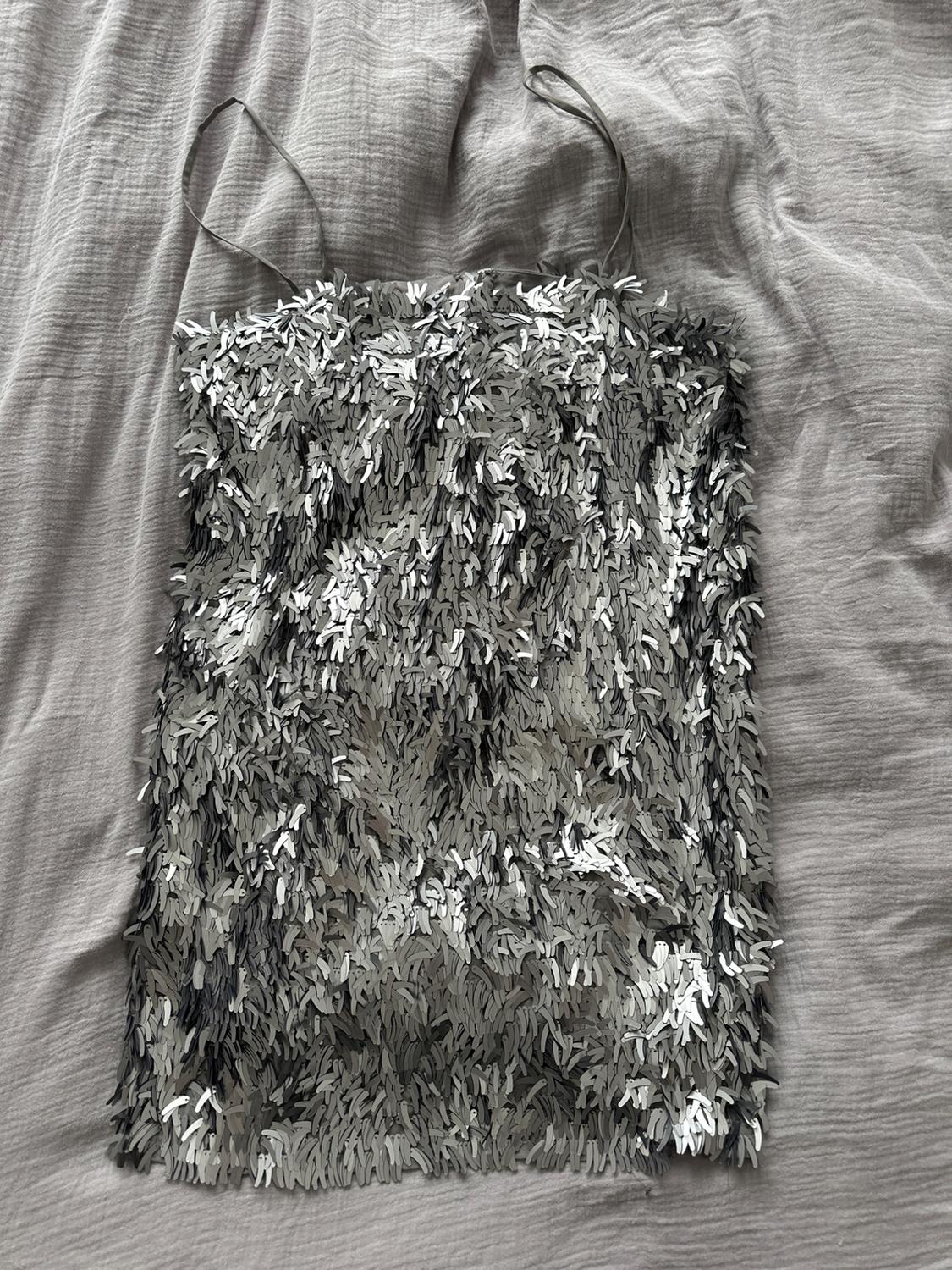 Silver sequin cami top on crinkled grey fabric. Shimmering, textured design.
