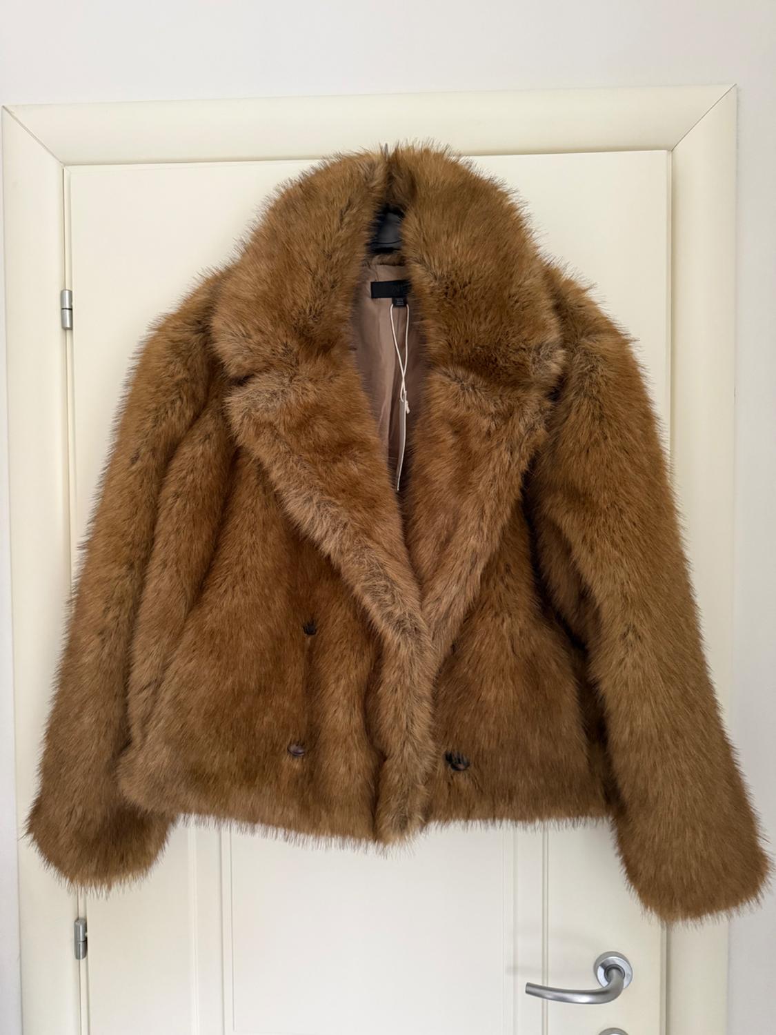 Brown faux fur coat hanging on a white door. Double-breasted design and wide collar.