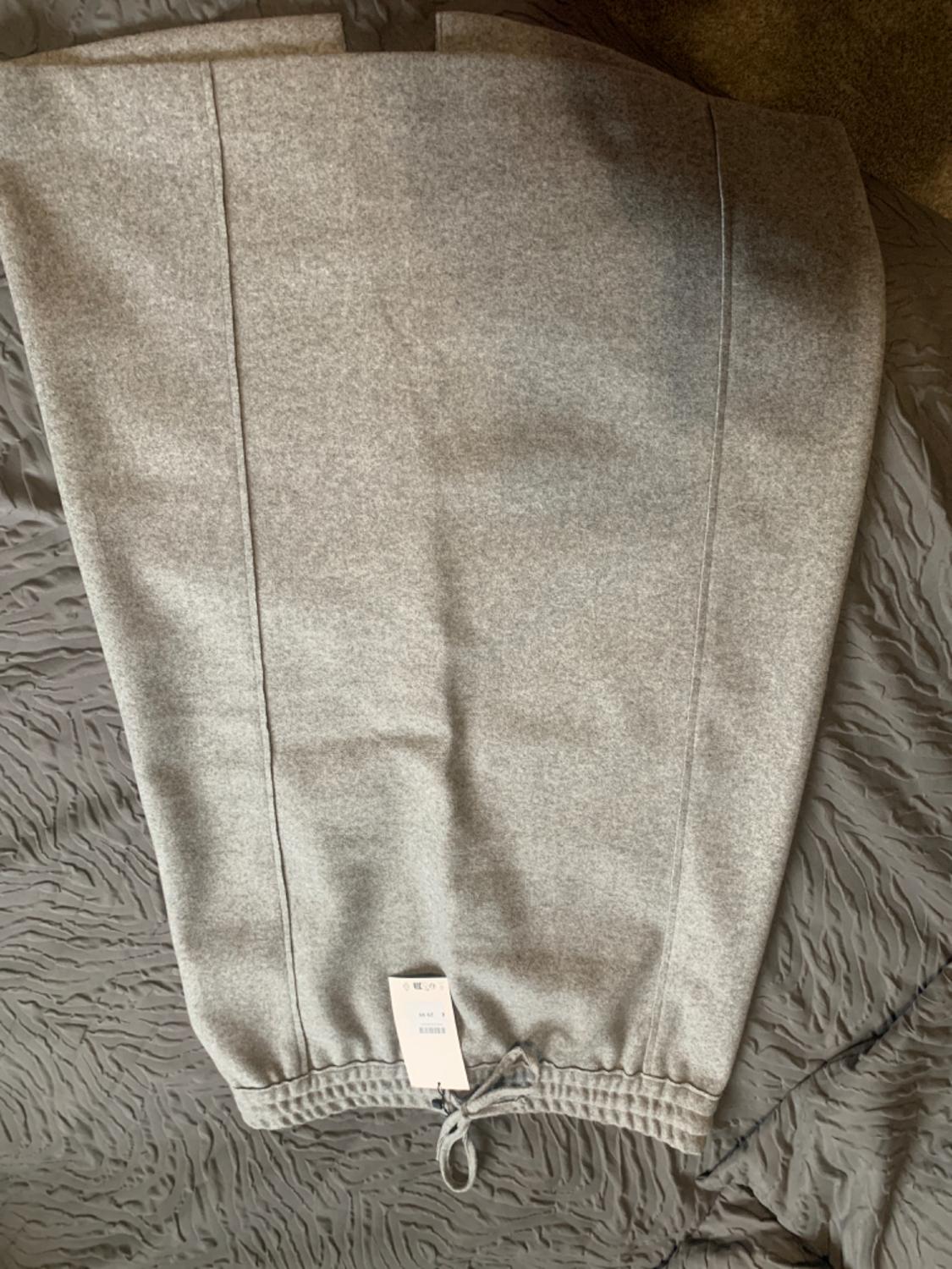 Grey soft-fabric trousers with drawstring waistband, on a textured grey bedspread. Visible label at the bottom.