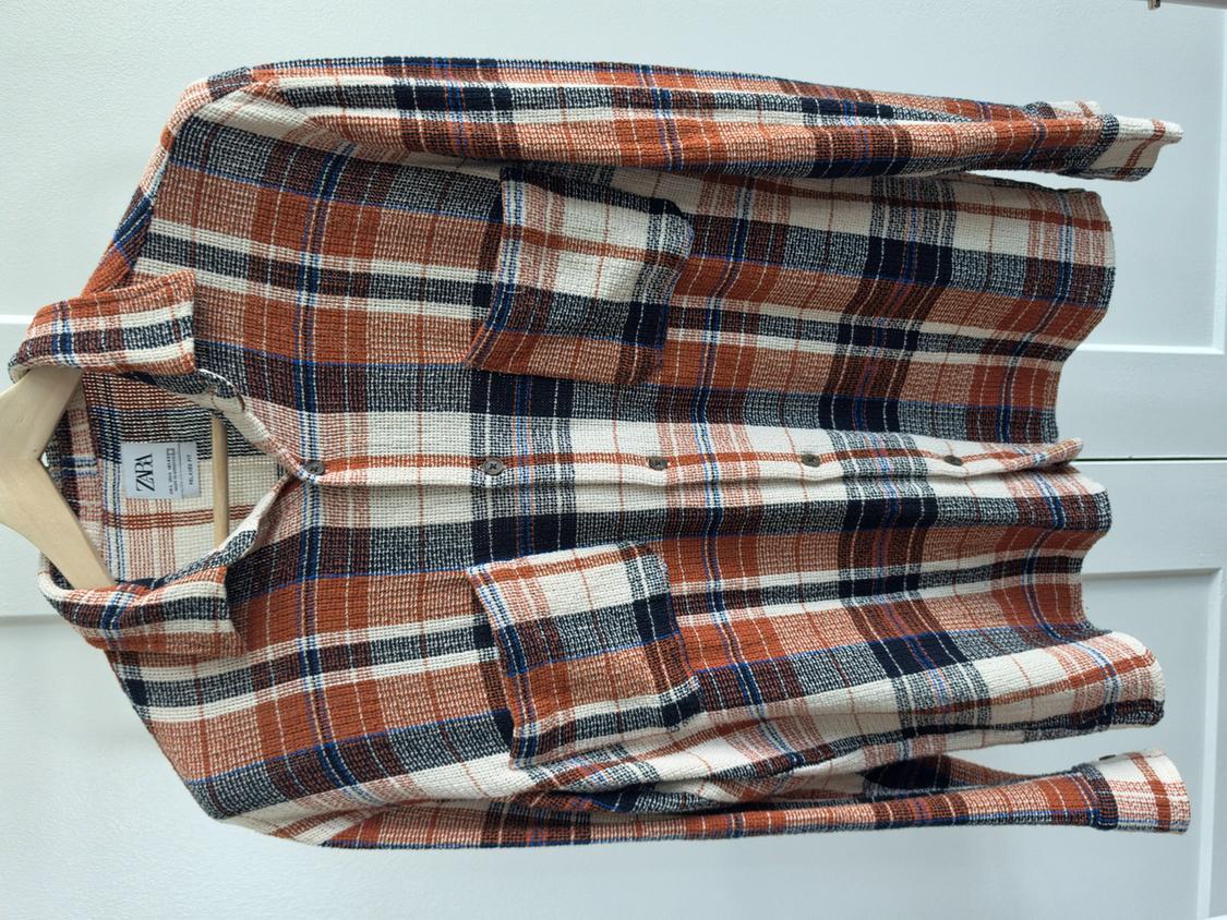 Long-sleeved orange, blue, and plaid shirt on a wooden hanger against a white background. Label with ZARA text visible.