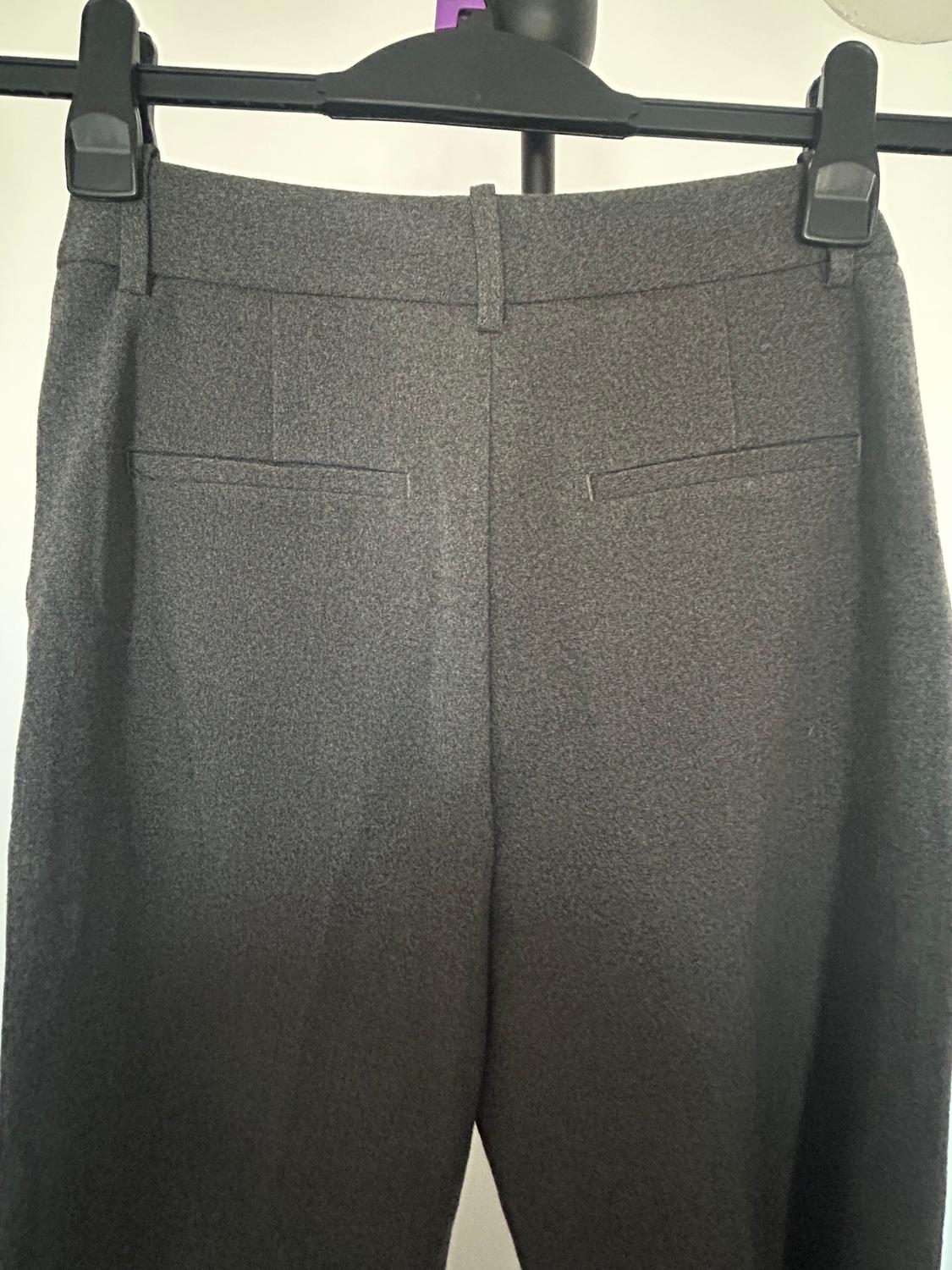 Grey trousers hanging on a black hanger, showing the back with pockets and belt loops. White background.