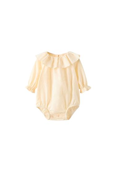 Front view of beige bodysuit with ruffled collar and long sleeves.