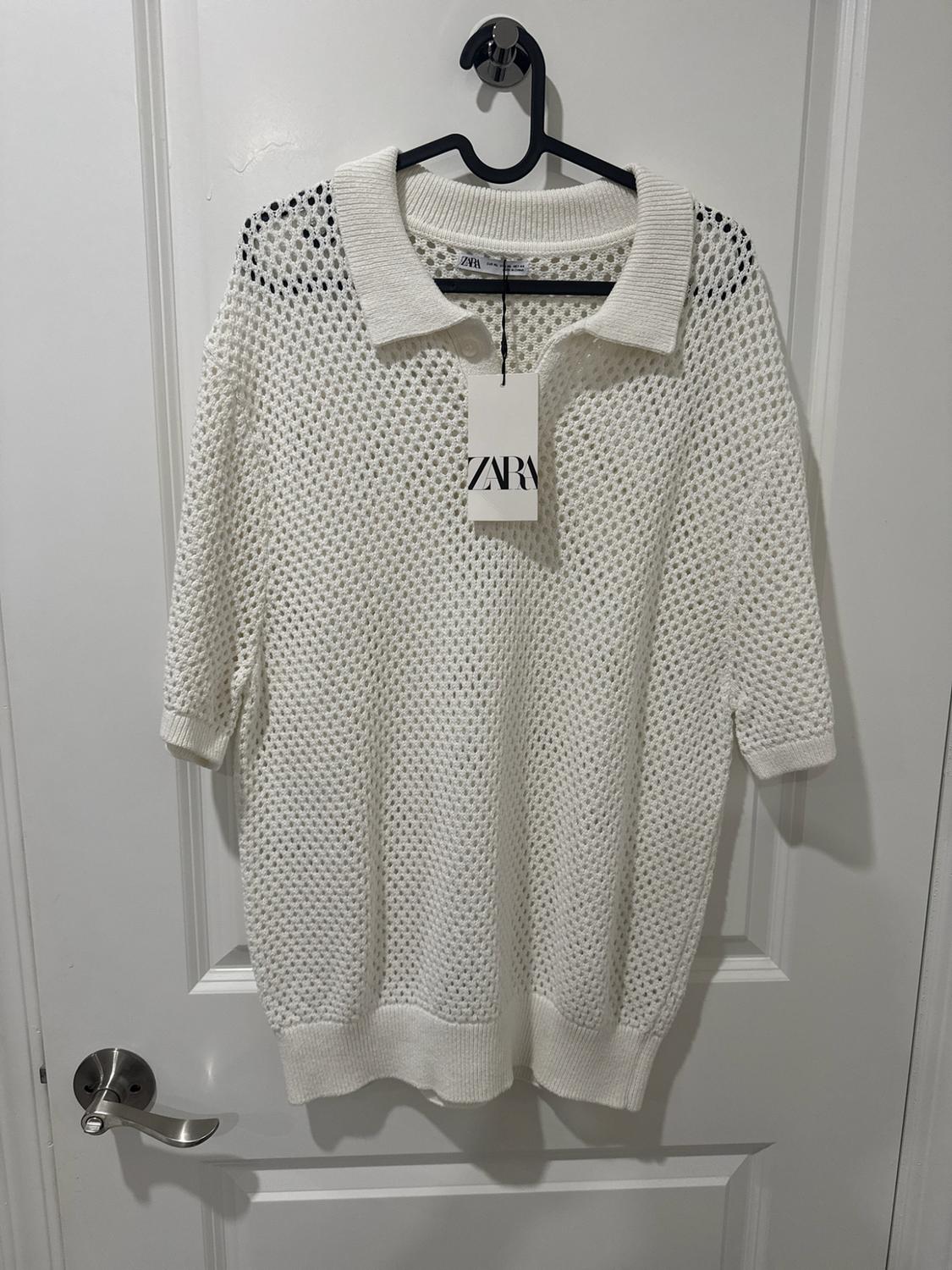 White short-sleeve open-knit polo shirt hanging on a white door. Visible tag with the text ZARA.