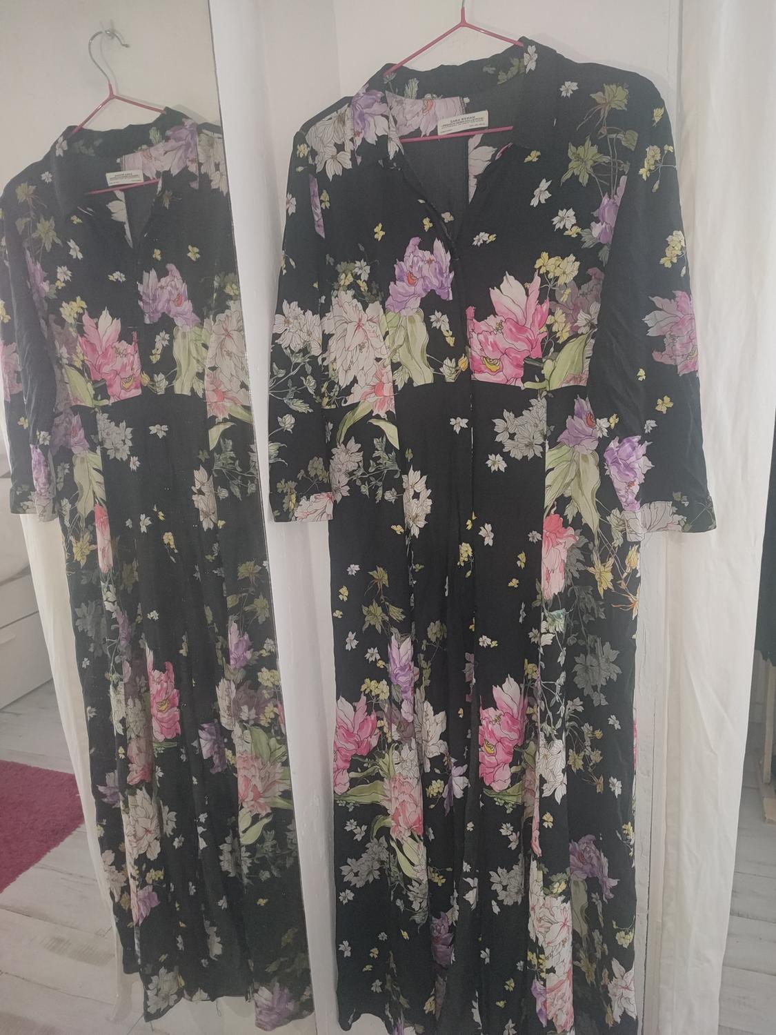 Black dress with a floral print in pink, lilac, and green tones, hanging on a hanger and reflected in a mirror.