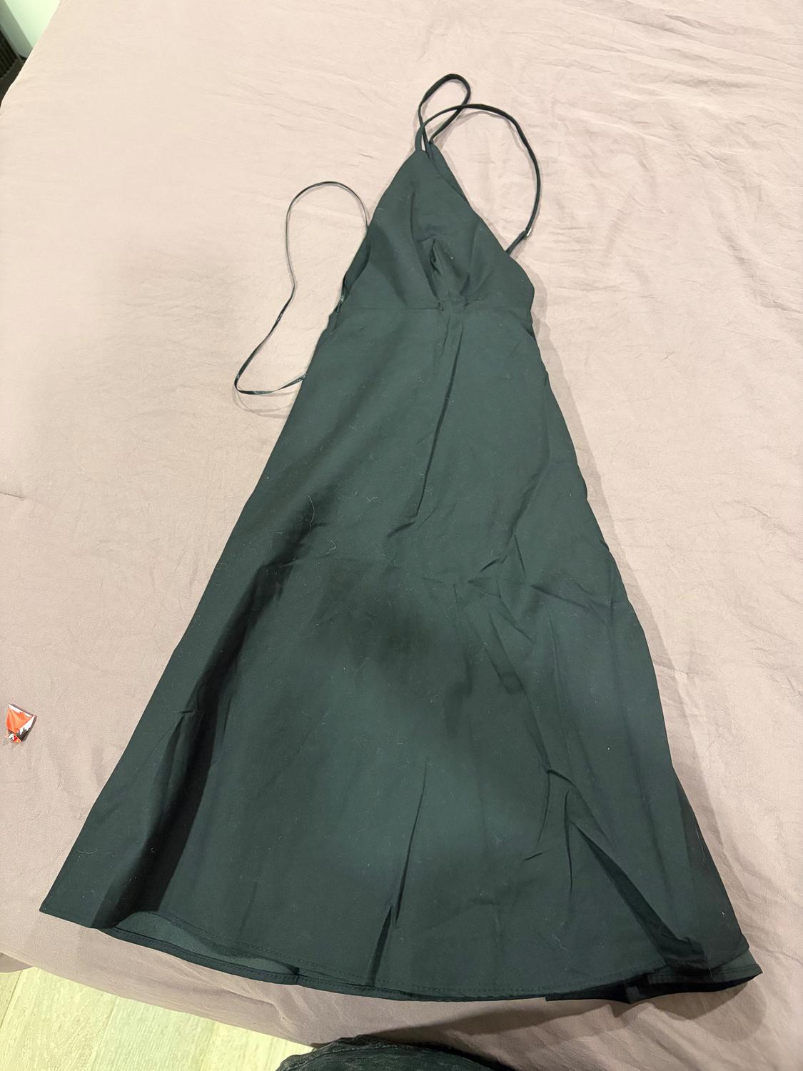 Black spaghetti strap dress on a bed with a beige sheet.