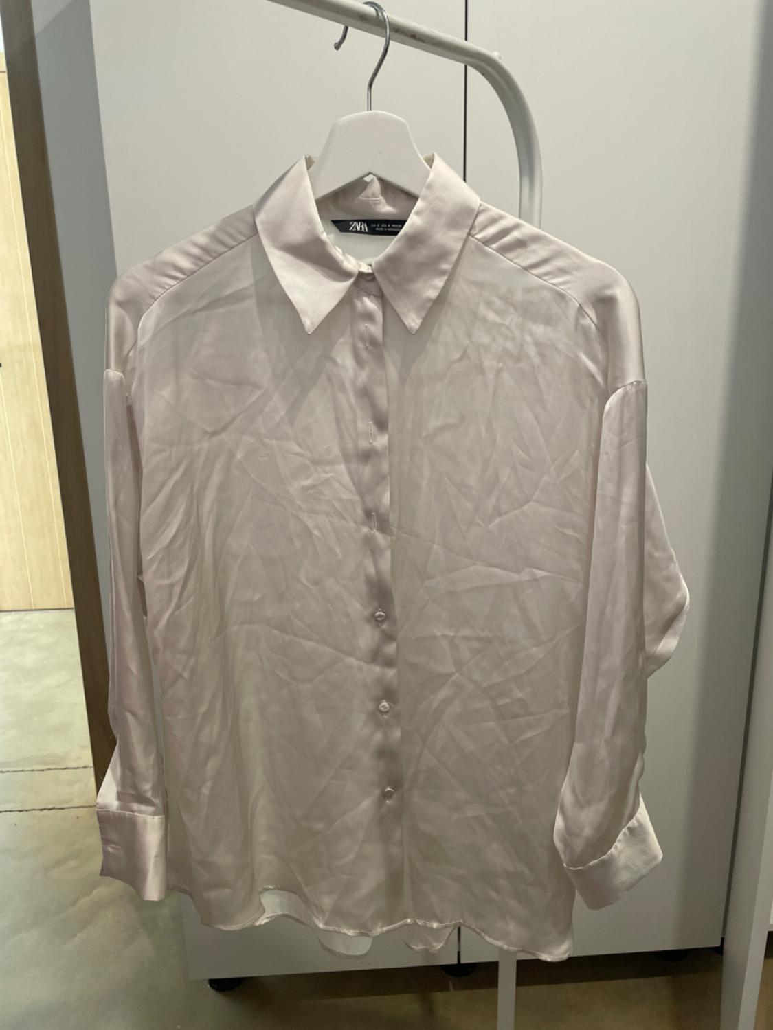 Creased white silk shirt hanging on a white hanger, with a wardrobe background and light wooden floor.