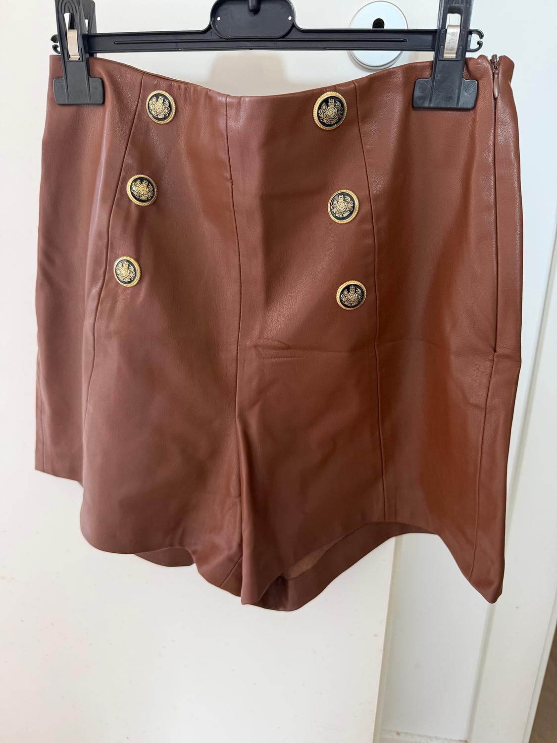 Brown shorts hanging on a hanger, with six decorative gold buttons on the front. White background.