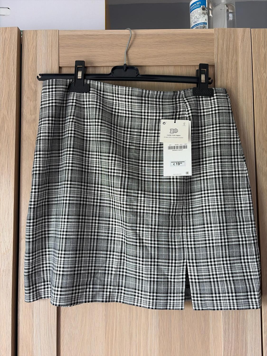 Black and white checked skirt with a slit, hanging on a wooden door. Text: CARE FOR FIBER At least 25% recycled polyester £19.95