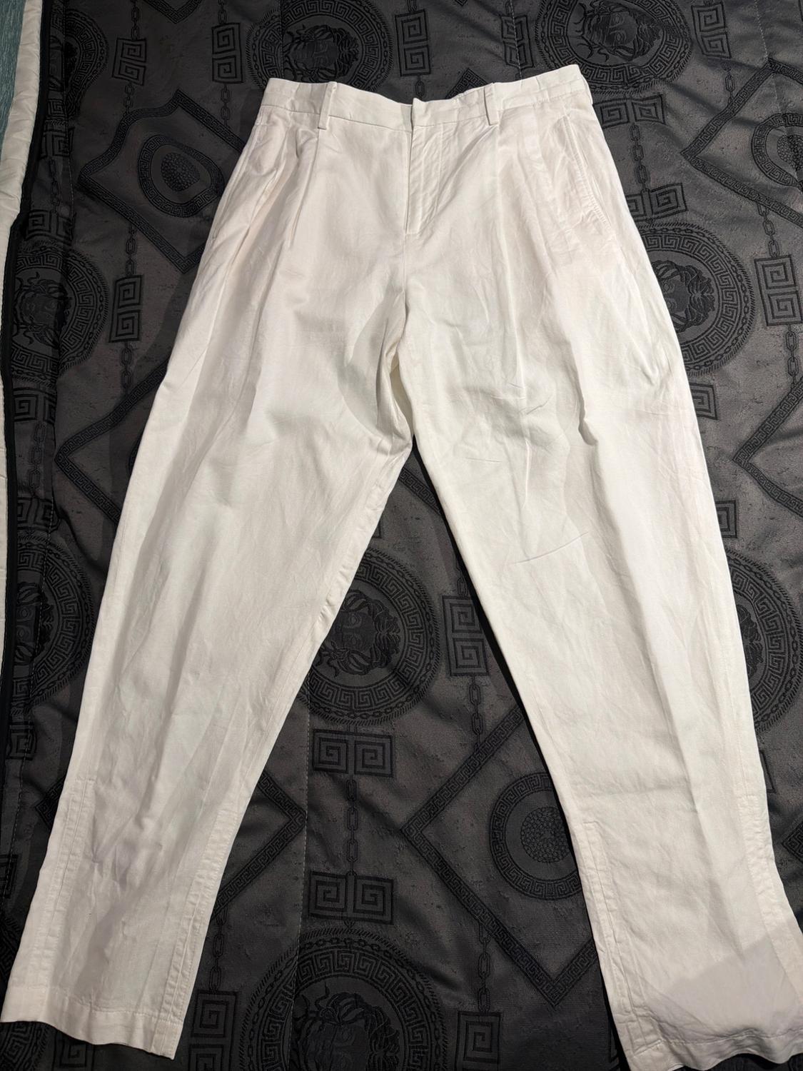 Light-coloured trousers made from a lightweight fabric on a dark bedspread with geometric patterns and lion details.