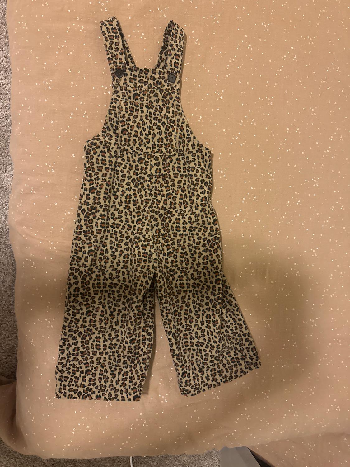 Leopard print children's jumpsuit on a beige background with small white dots. Soft fabric and buttons on the straps.
