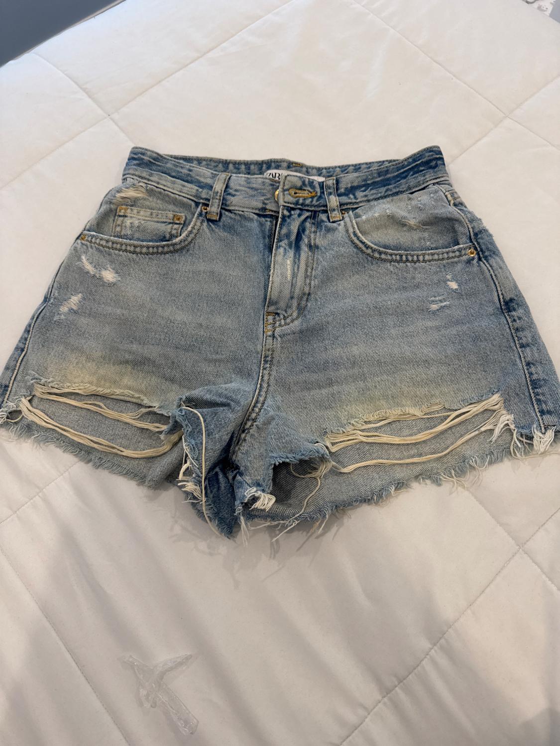 Distressed denim shorts with a frayed hem and ripped details, on a quilted white bedspread.