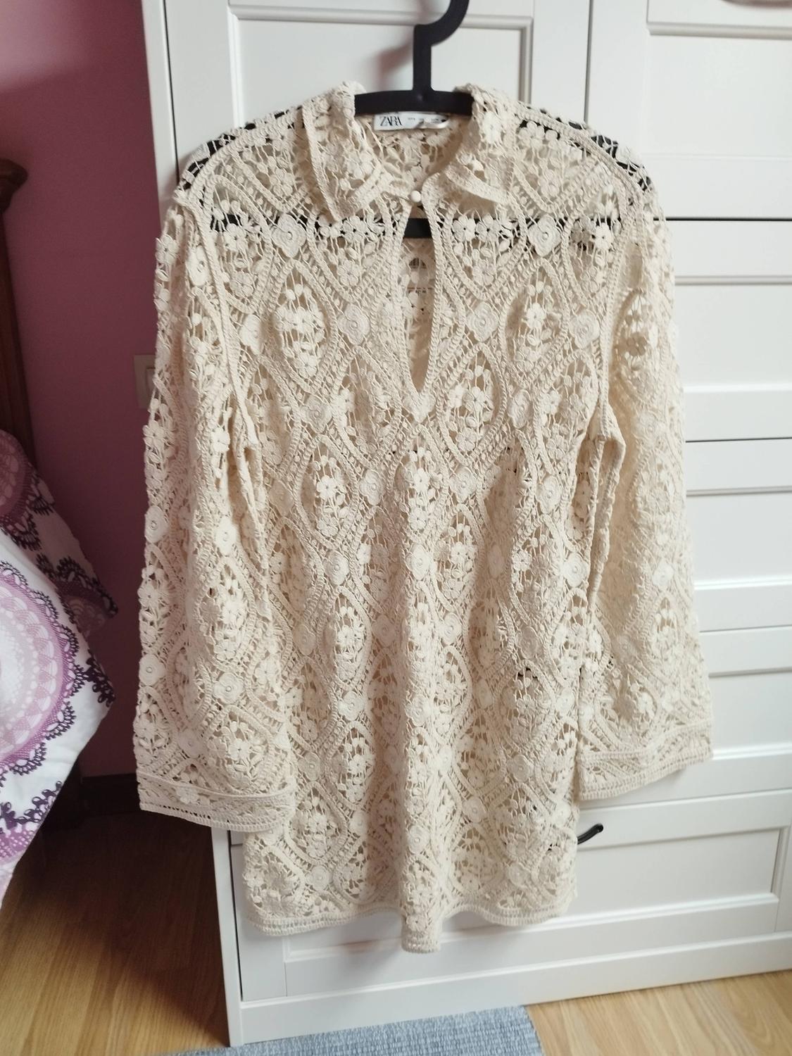 Beige lace dress hanging on a black hanger in front of a white wardrobe. Floral pattern detail and button-up collar.