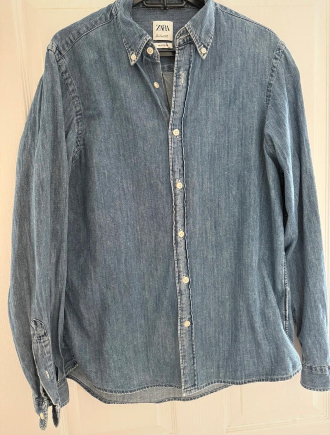Light blue denim shirt with white buttons, hanging on a hanger. Visible label with the text "ZARA".