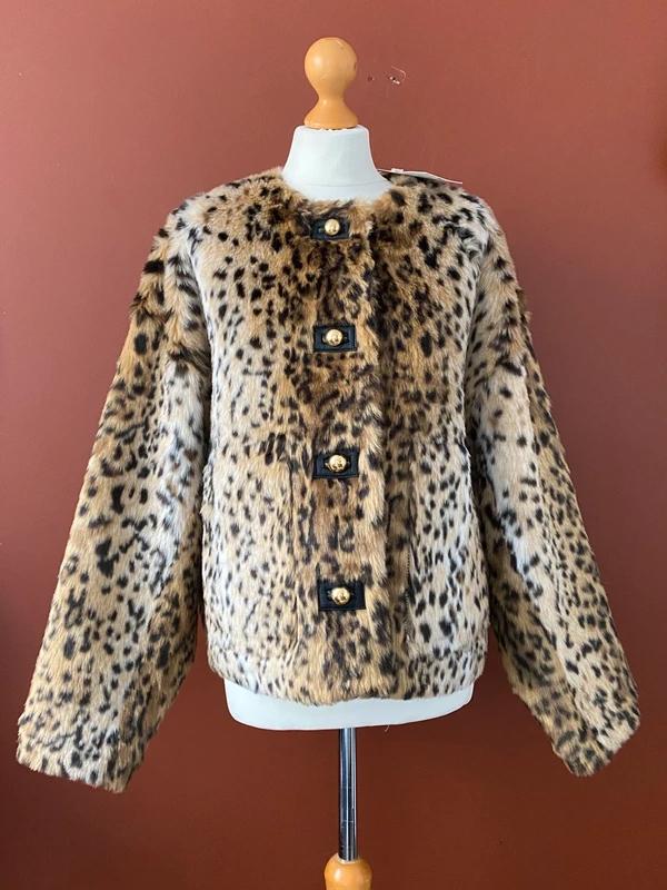Faux fur leopard print coat with large buttons on a mannequin, brown background.