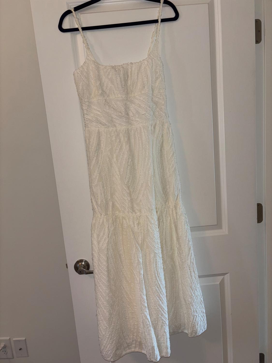 White dress with thin straps hanging on a black hanger over a white door. Fabric with a crinkled texture.