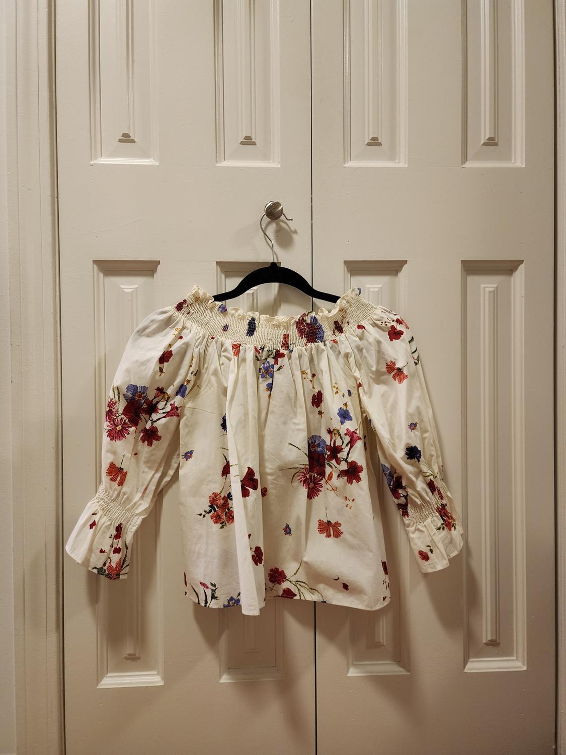 Front view of a white blouse with a red and blue floral print, long puffed sleeves, and a gathered neckline.