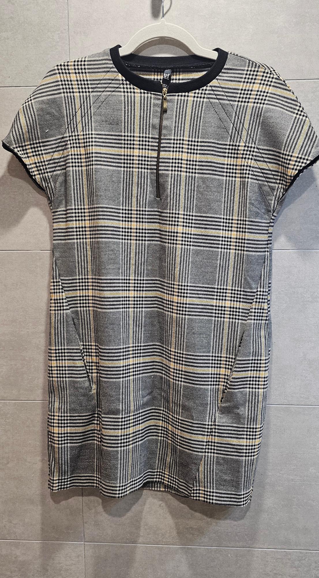 Grey and beige checked dress with a front zip, hanging on a hanger against a grey tiled background.
