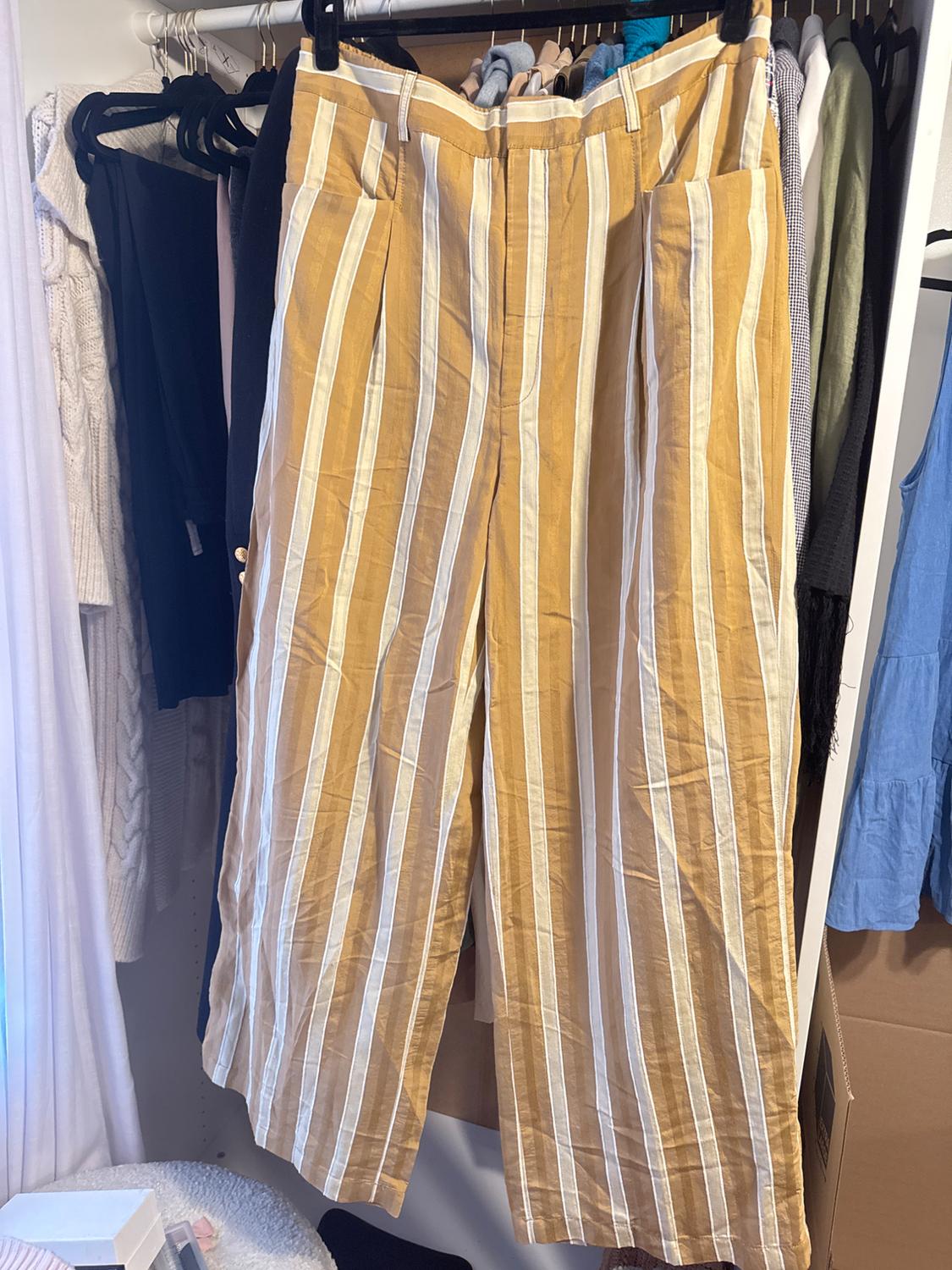 Yellow and white vertically striped trousers hanging in a wardrobe, surrounded by other garments of various colours.