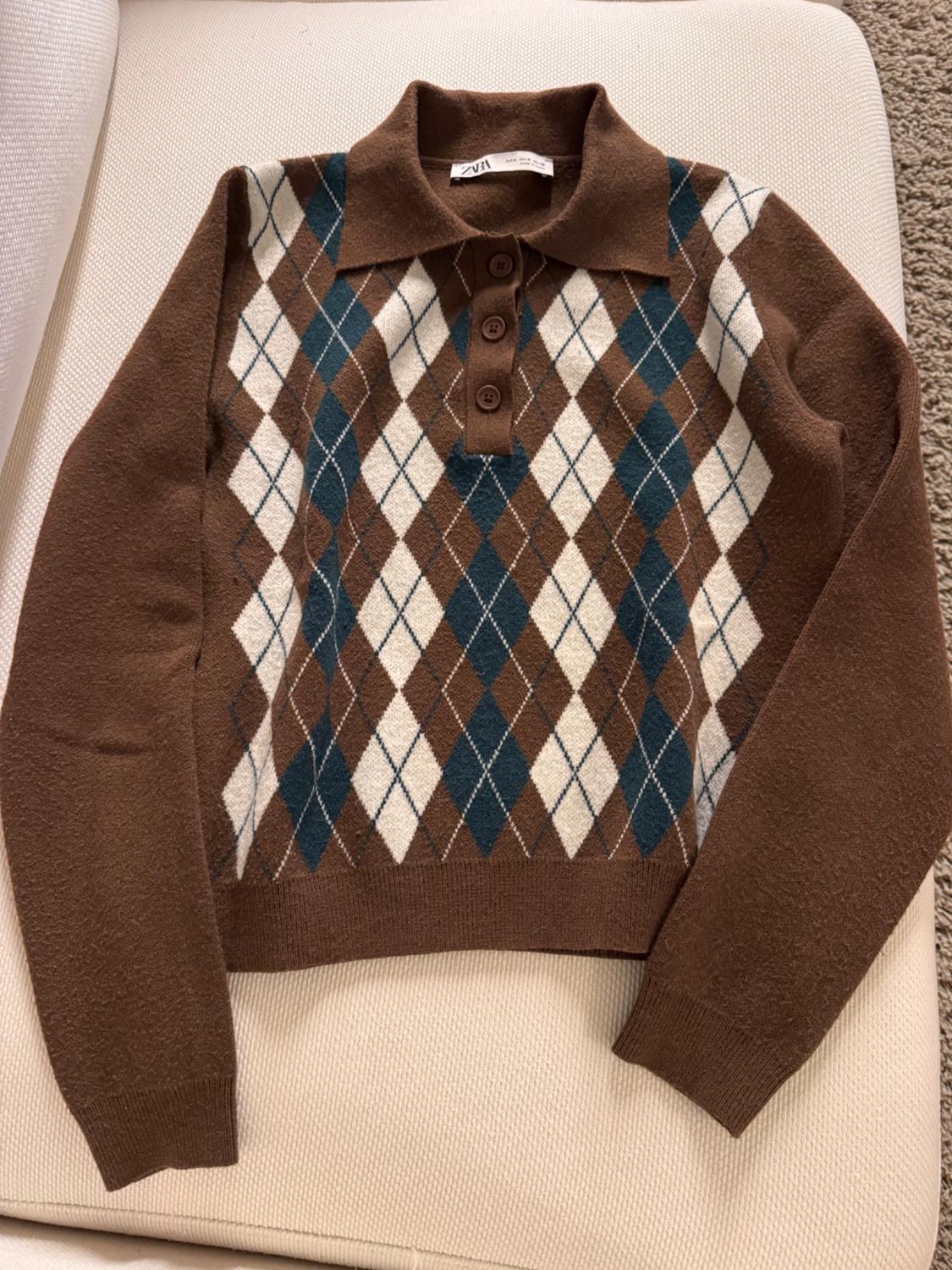 Brown jumper with a white and blue argyle pattern, polo neck, and brown buttons, on a light background. Visible label: "ZARA".