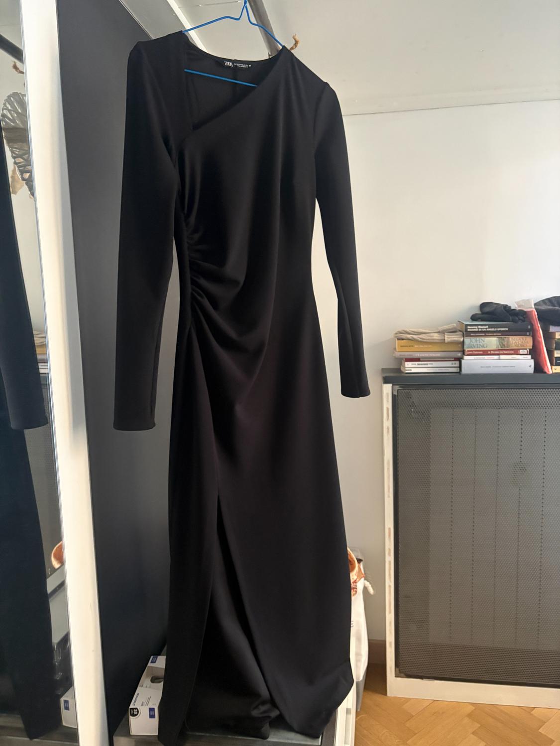 Long-sleeved black dress hanging on a blue hanger, with books stacked on a piece of furniture in the background.