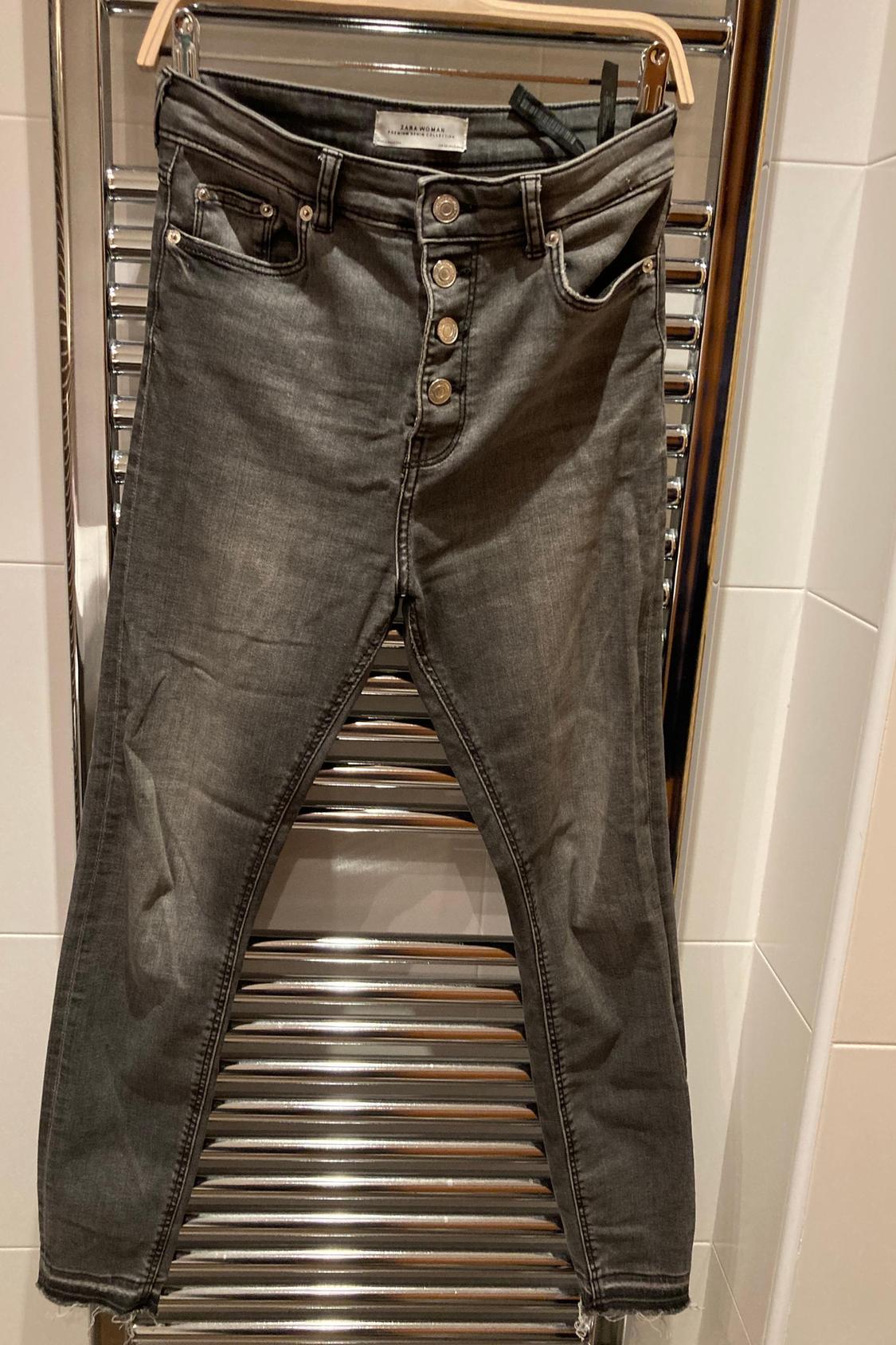 Front view of grey jeans with a visible button fly and front pockets.