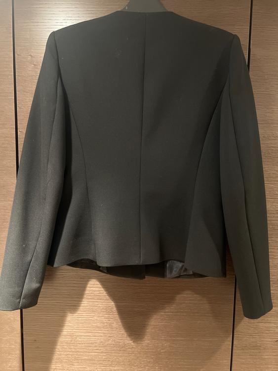 Black suit jacket hanging on a hanger, viewed from the back, against a light brown wooden background.