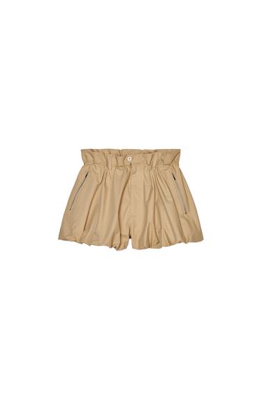 Front view of beige shorts with a ruffled elastic waistband and zippered side pockets.