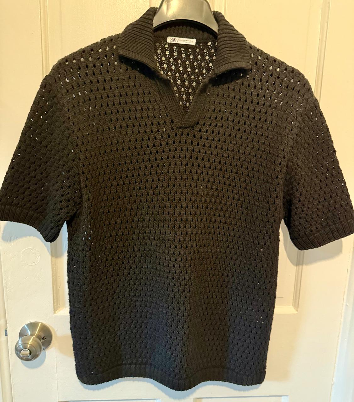 Dark open-knit sweater with a polo collar and short sleeves, hanging on a hanger over a white door.