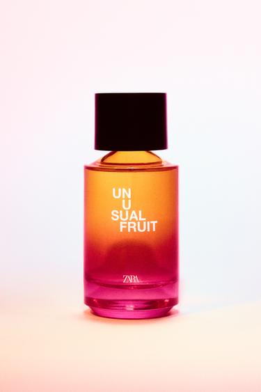 Parfümflasche mit dem Text "UNUSUAL FRUIT" auf Farbverlaufglas von Orange zu Rosa, schwarzer Verschluss.