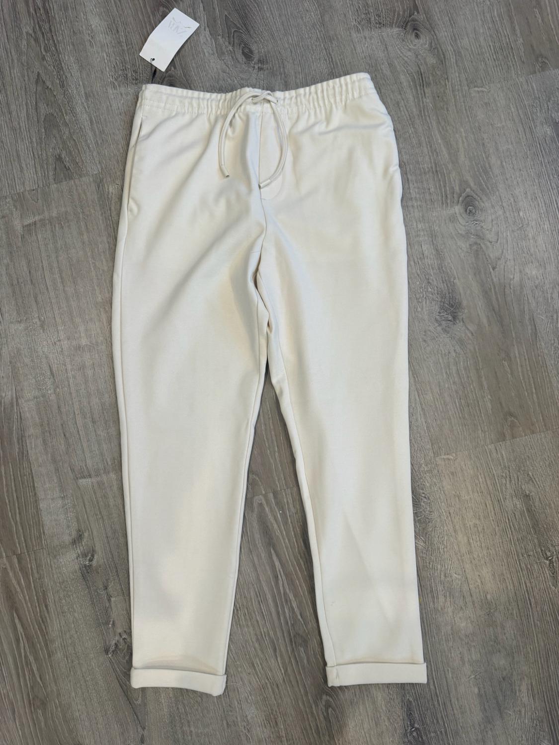 Beige jogger trousers with an elasticated waist, drawstring and turned-up hems on a wooden floor. Label with ZARA text.