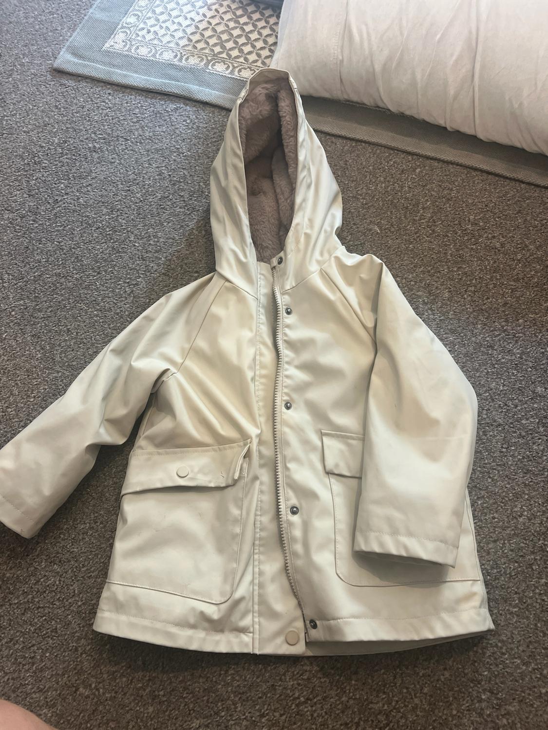 Light beige jacket with a soft brown lined hood, zip fastening and flap pockets, on a grey rug.