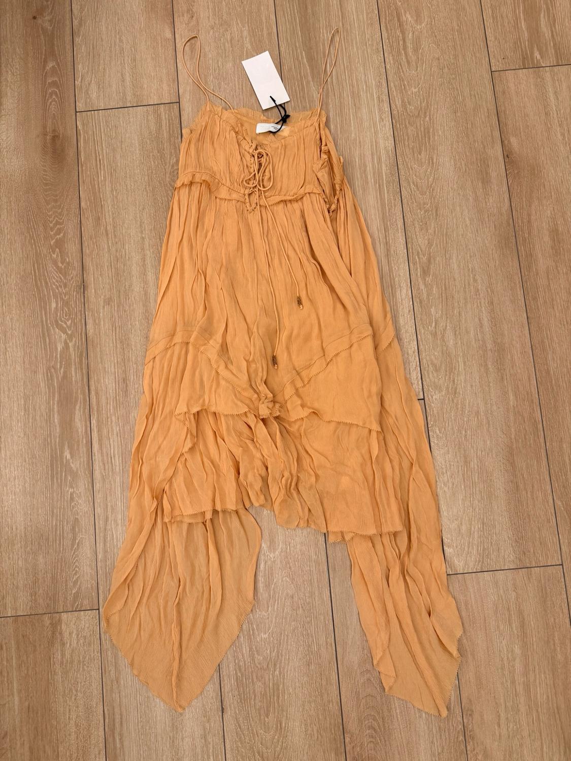 Light orange spaghetti strap dress with a lace-up neckline and an asymmetric frilled hem, laid out on a wooden floor.