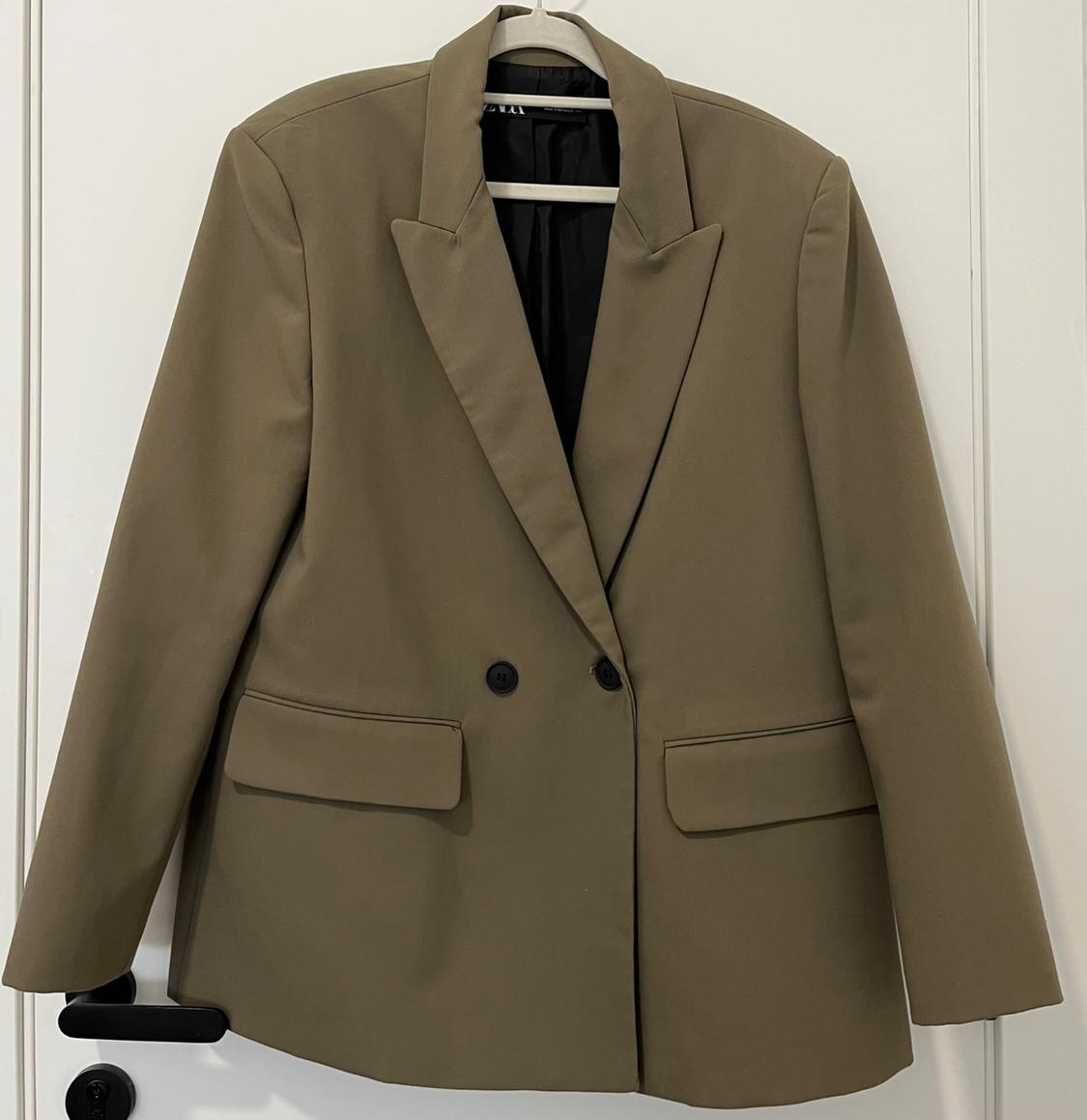 Beige two-button jacket hanging on a white hanger over a white door.