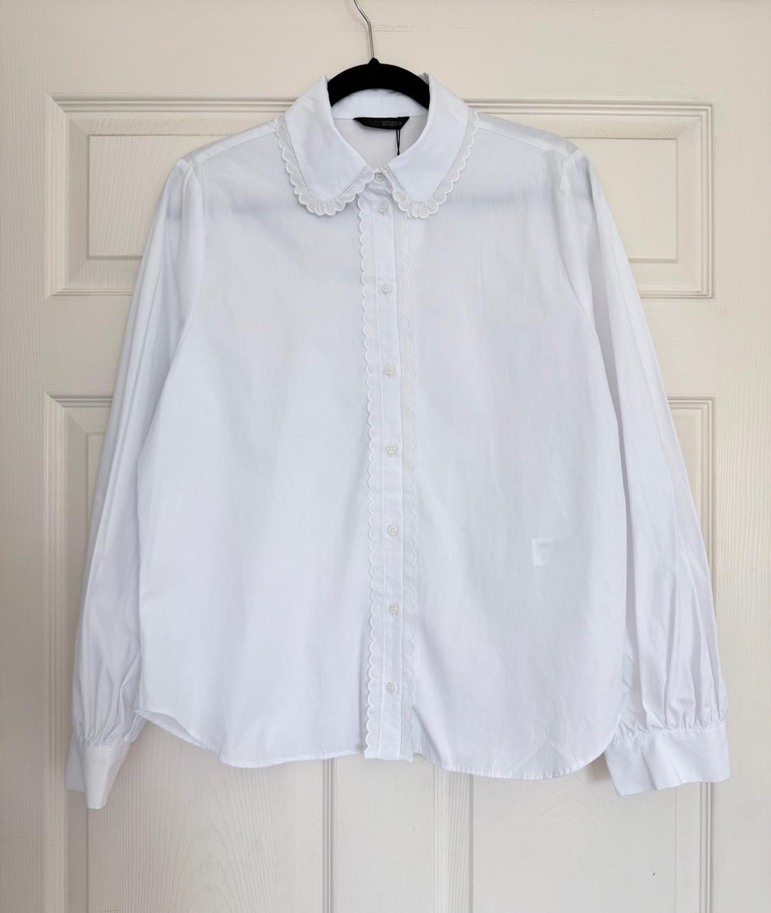 White long-sleeve shirt with a scalloped collar and button placket, hanging on a black hanger on a white paneled door.
