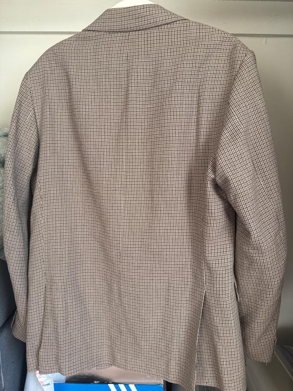 Brown plaid jacket hanging on a coat rack, seen from behind. Neutral background with part of a blue box visible below.