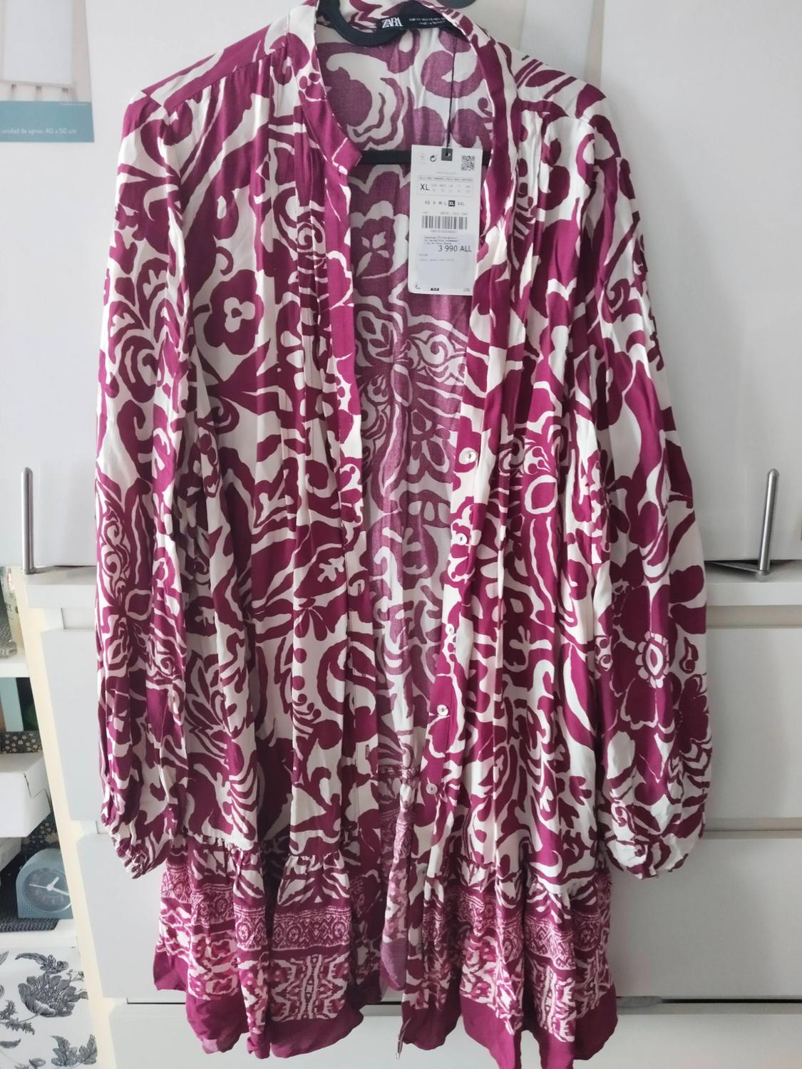 White long-sleeved dress with magenta print hanging in a wardrobe. Visible text: ZARA XL 3 990 ALL. Relaxed atmosphere.