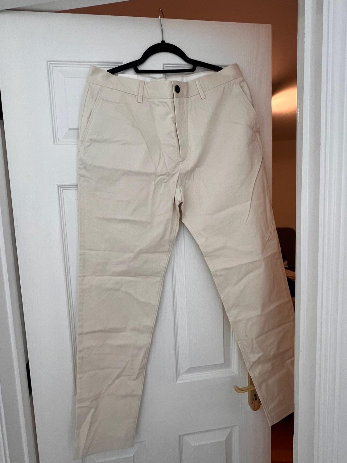 Light beige trousers hanging on a black hanger on a white, slightly open door. Casual style in a relaxed, homely setting.