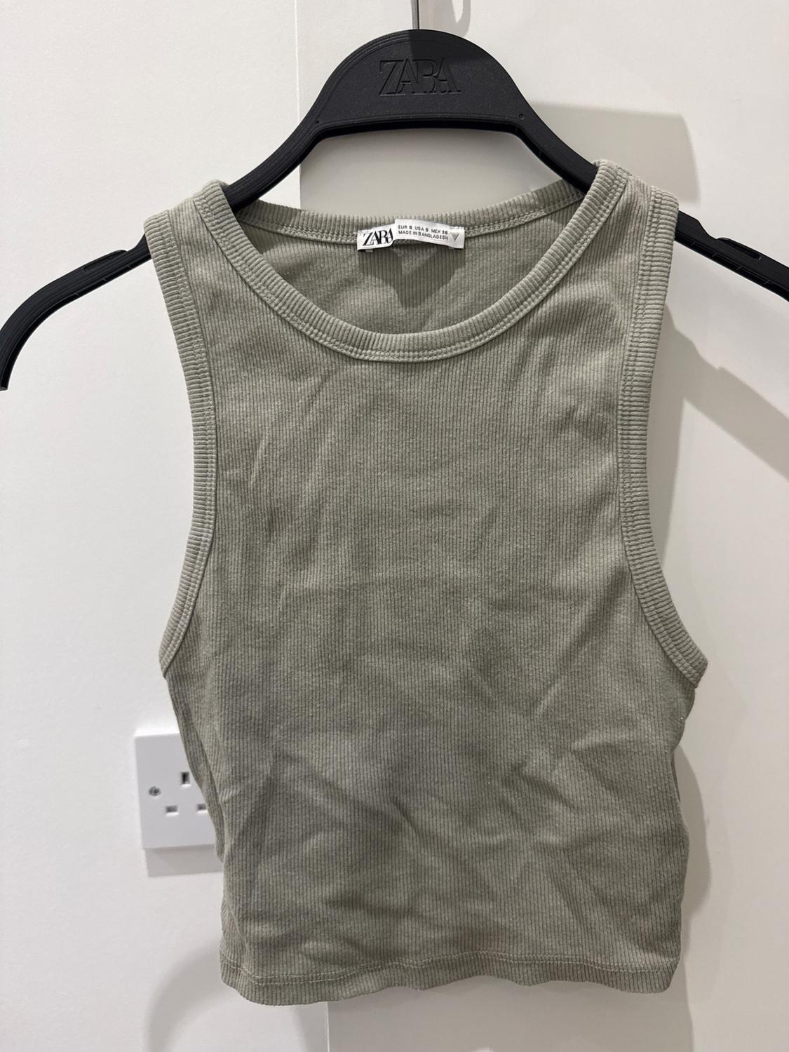 Light grey sleeveless top on a black hanger with Zara logo. White background with visible plug socket on the left.