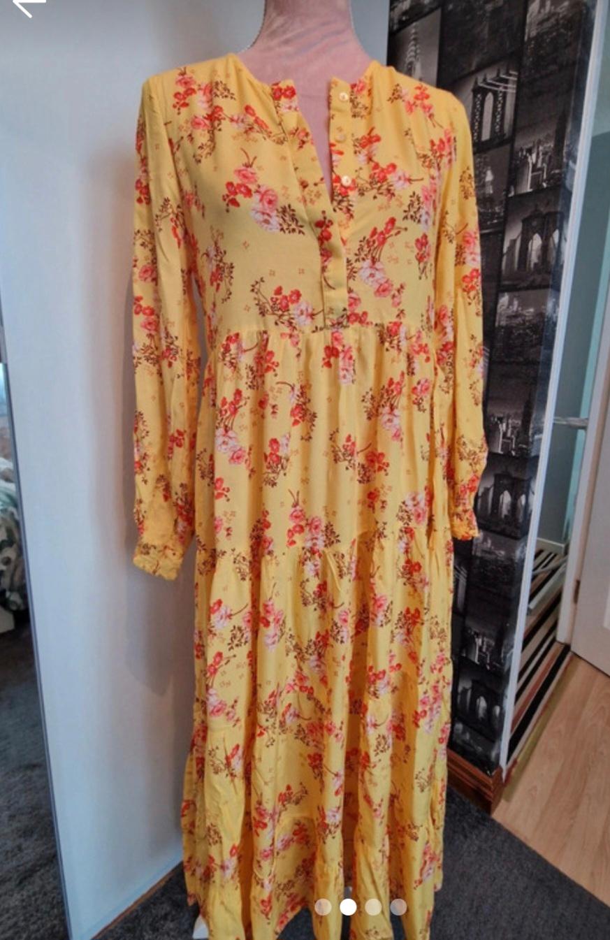 Yellow dress with red and pink floral print, long sleeves and front buttons, displayed on a mannequin in an indoor setting.