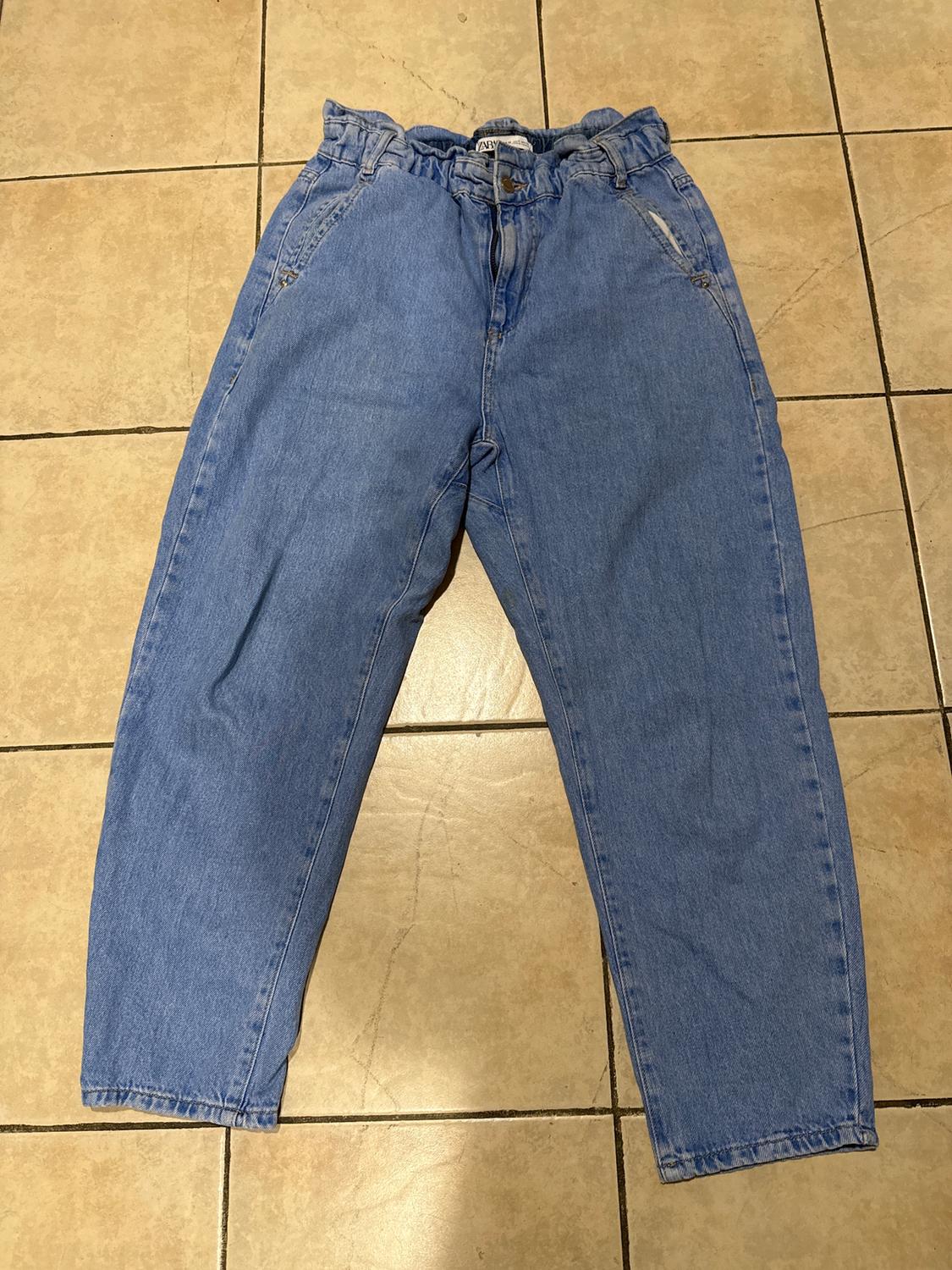 High-waisted blue jeans with elastic at the top, placed on a beige tile floor.