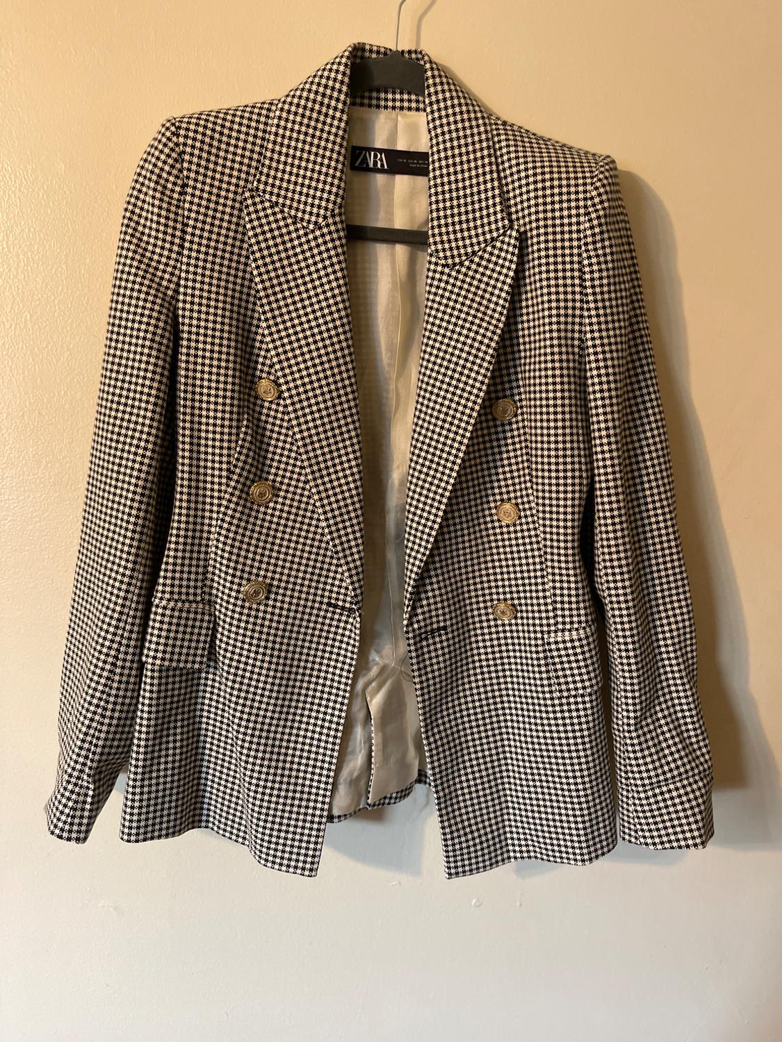 Black and white plaid jacket with double-breasted gold buttons, hanging on a hanger. Visible tag: ZARA.